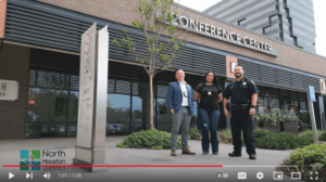 Screen capture of YouTube video from the 2023 Blue Star Training outsinde an office complex conference center featuring three police officers, one man dressed in a sharp blue suit, a pretty female officer in street clothes with wearing a lanyard-style badge and a uniformed police officer smiling. 